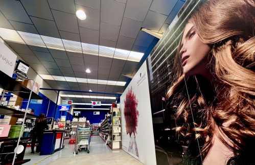 Imagen de interior de almacén con estantes con productos y pared con imagen de peluquería en vinilo